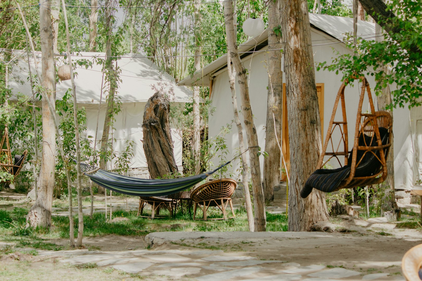 Quiet outdoor setting with a hammock and wicker chair amidst trees. Nearby, a white cabin is partially visible, creating a serene, relaxed atmosphere. Symbolising digital detox and slow travel