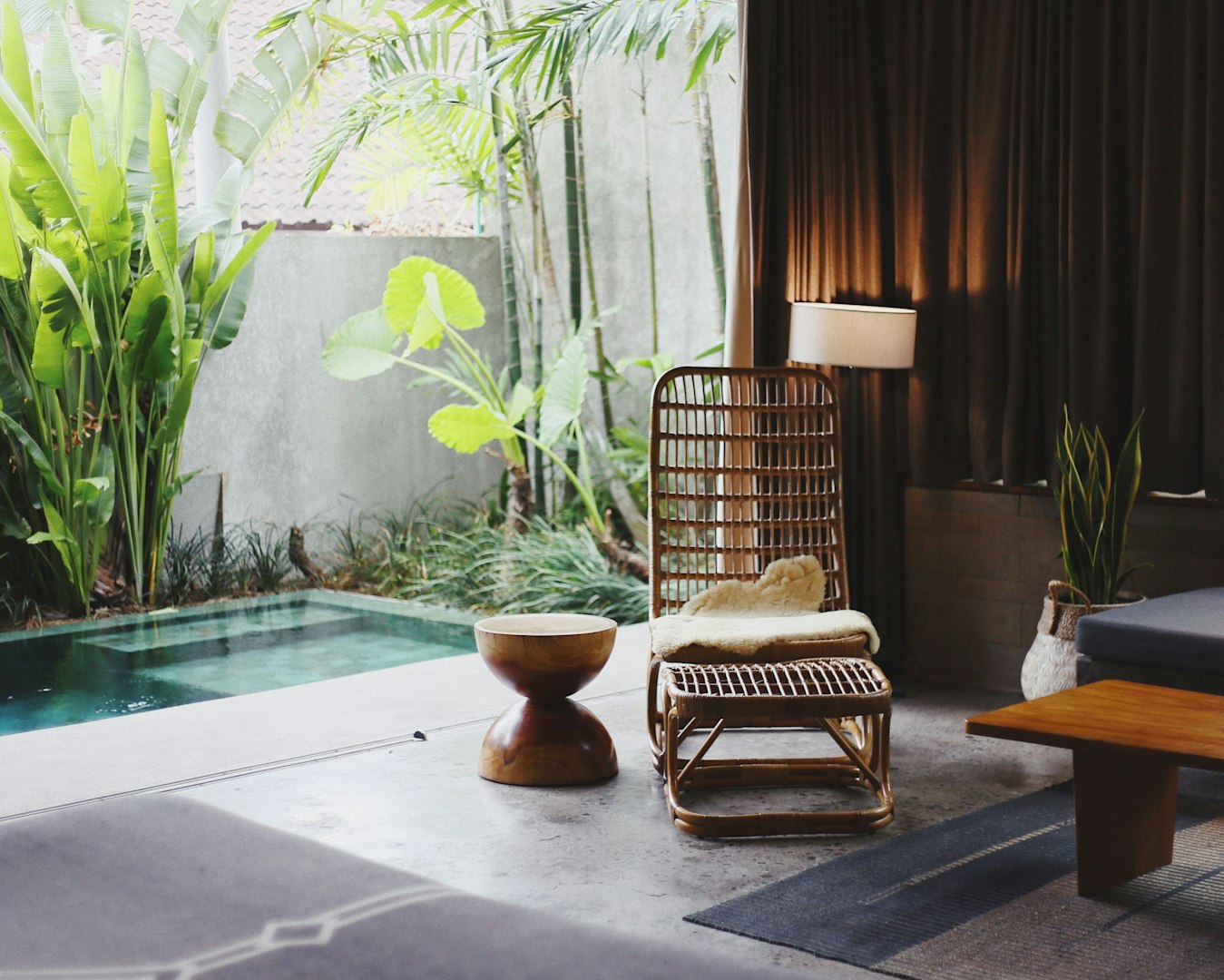 Stylish room with rattan chair, wooden side table, and indoor plants near a small pool. Soft lighting and lush greenery create a tranquil vibe in thermal spa and nature lodges and accommodations. 